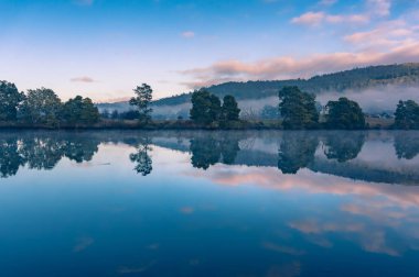 Güneşin doğuşundaki su yüzeyi gibi aynalı sakin bir manzara.