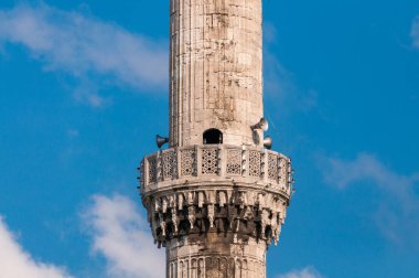 Minaret tower with megaphones attached against blue sky on the b
