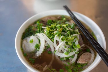 Vietnamlı Pho çorbasını yemek çubuklarıyla bir kaseye koy.