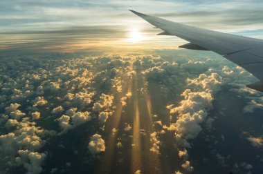 View from airplane side window on sunset sky and sunlit clouds