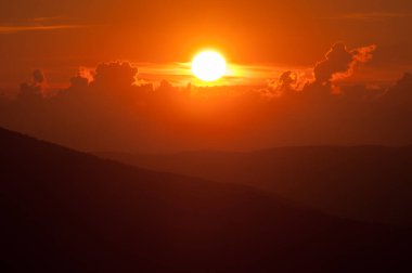 Canlı turuncu gökyüzü ve tepeleriyle destansı gün batımı manzarası