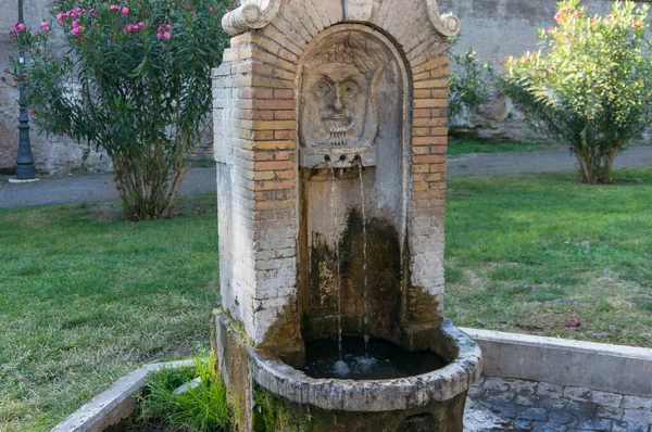 Old drinking fountain with stylized face and flowing water — Stock Photo, Image