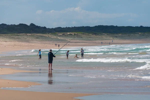 Playa de arena con pescador y gente bañándose y divirtiéndose — Foto de Stock