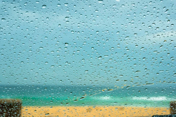 Zbliżenie szyby samochodowej z kroplami deszczu i piaszczystą plażą — Zdjęcie stockowe