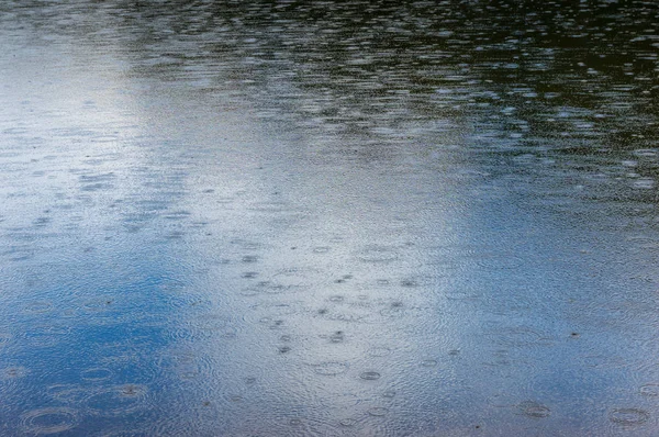 Lake, river surface with raindrops, water droplets and reflection of blue sky