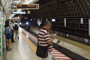 Tokyo metro istasyonu, tren geliyor ve kıdemli adam selam veriyor.