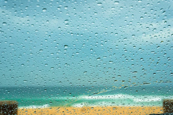 Primer plano del parabrisas del coche con gotas de lluvia y playa de arena — Foto de Stock