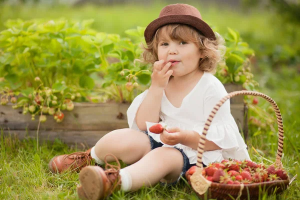 Aranyos kislány eper ül a greeb füvet eszik. — Stock Fotó