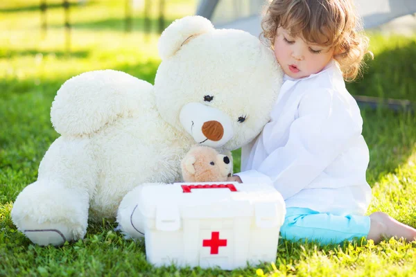 toddler girl playing doctor with plush toy bear outdoors