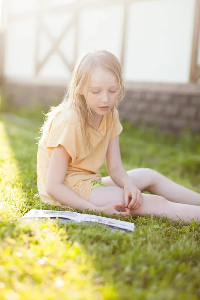 Hermosa adolescente leyendo libro y sentado en la hierba verde — Foto de Stock