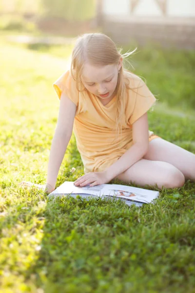 Красивая девочка-подросток читает книгу и сидит на зеленой траве — стоковое фото
