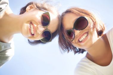 İki sevimli kız gülümseyerek, güneş gözlüğü takıyor