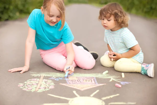 Kleine Schwestern malen draußen mit Farbkreide. Kreidezeichnungen Stockbild