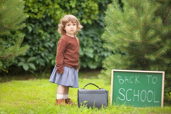 Adorable niña pequeña; de vuelta a la escuela escrito en tiza blackboar — Foto de Stock