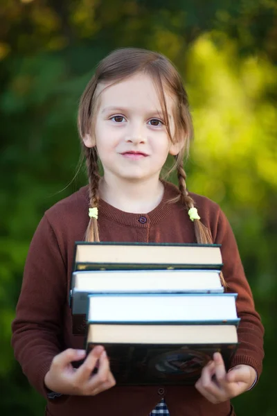 Niña preescolar sosteniendo pila de libros y sonriendo . — Foto de Stock