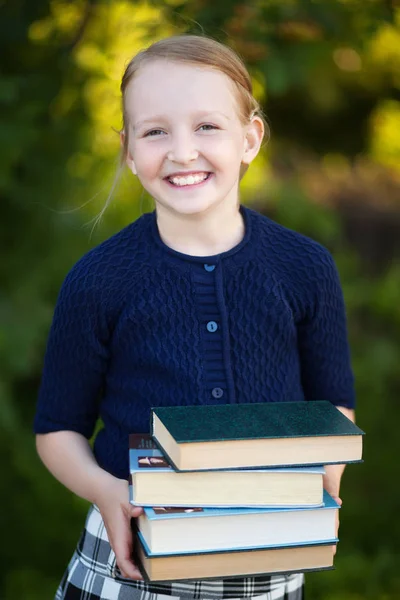 Adolescente colegiala sosteniendo pila de libros y sonriendo — Foto de Stock