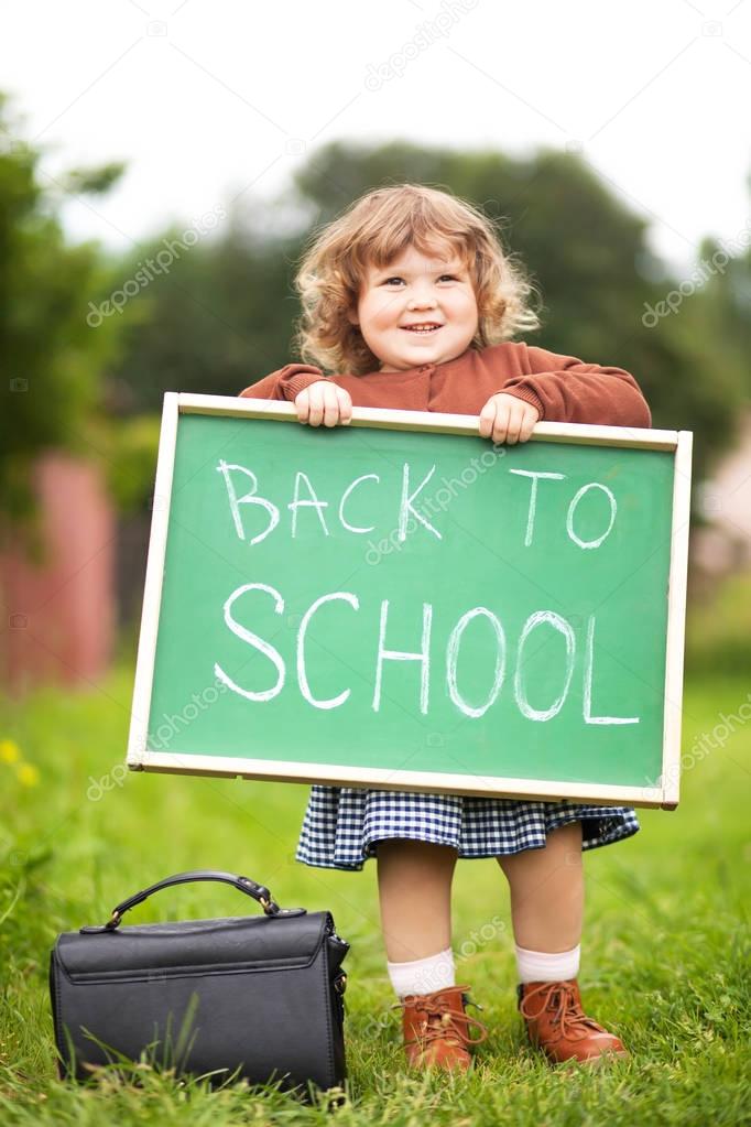 Adorable smiling toddler girl with back to school text blackboard