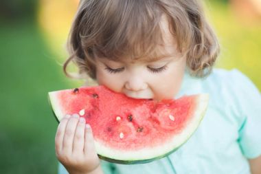 Sevimli küçük kız bir dilim karpuz açık havada yiyor