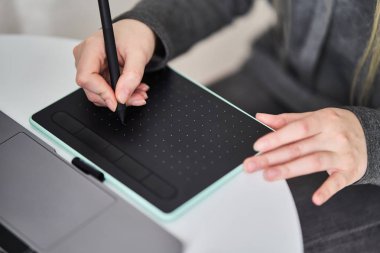 Genç bir kız grafik tabletine resim çiziyor. Freelancer bir kafede çalışıyor.