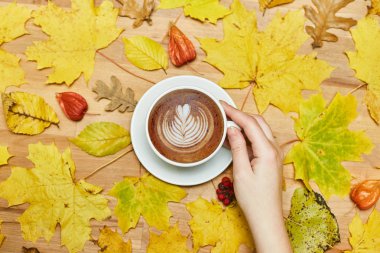 Sonbahar düz kompozisyonu kuru yapraklar çelenk çerçeve ve kadın elinde latte fincanı ahşap zemin üzerinde. 