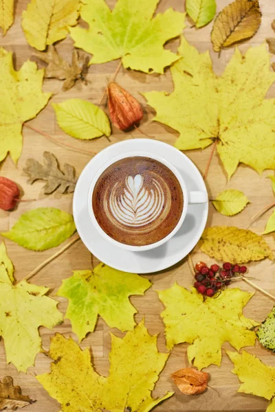 Composición plana de otoño con marco de corona de hojas secas y taza de café con leche sobre fondo de madera . — Foto de Stock