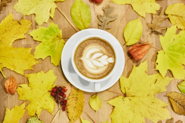 Composición plana de otoño con marco de corona de hojas secas y taza de café con leche sobre fondo de madera . — Foto de Stock