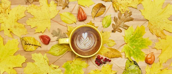 Composición plana de otoño con marco de corona de hojas secas y taza de café con leche sobre fondo de madera . — Foto de Stock