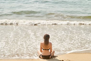 Genç bir kız sahilde dinleniyor. Kız yoga yapıyor.