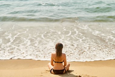 Genç bir kız sahilde dinleniyor. Kız yoga yapıyor.