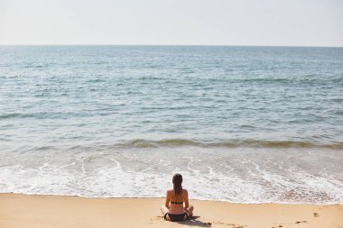 Genç bir kız sahilde dinleniyor. Kız yoga yapıyor.