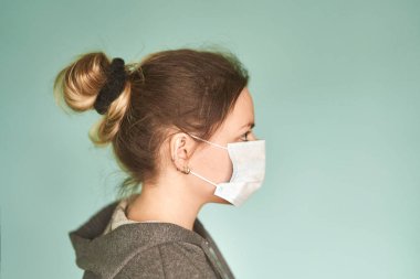 Yeşil arka planda tıbbi maskeli bir kız. Coronavirus. Viral hastalıkların önlenmesi