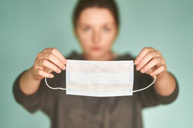 Kızın elinde tıbbi bir maske var.