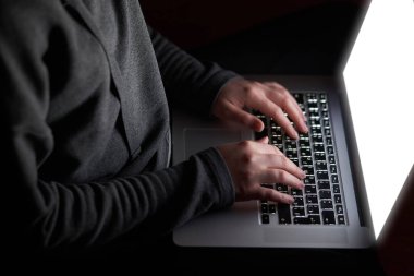 Overhead hacker in the hood working with laptop typing text in the darkroom. 