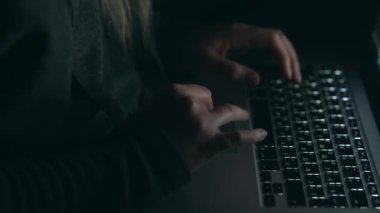 Overhead hacker in the hood working with laptop typing text in the darkroom. 