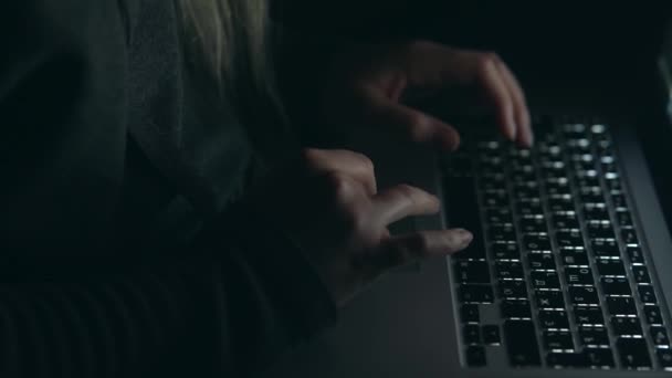 Накладний хакер у капоті, що працює з ноутбуком, що друкує текст у темній кімнаті . — стокове відео