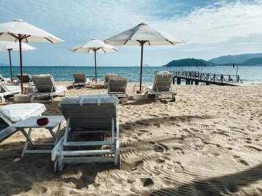 Kumlu bir sahil kıyısındaki beyaz, yumuşak güneş pansiyonları. Tropi