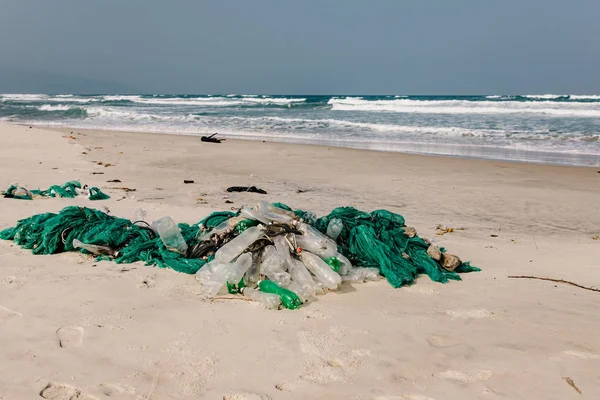 Plastik şişeler ve kumlu deniz kıyısına atılan diğer çöpler, deniz sahilindeki çöpler. Ekolojik bir sorun. Çevre kirliliği. Kirli kumsal. Kıyıya atılan eski bir balık ağı.,