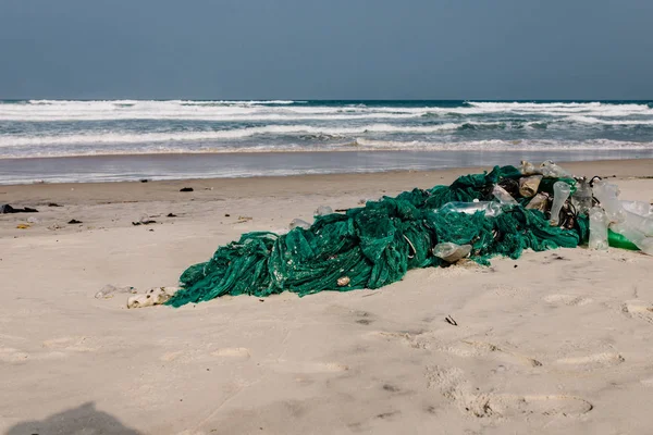 Plastik şişeler ve kumlu deniz kıyısına atılan diğer çöpler, deniz sahilindeki çöpler. Ekolojik bir sorun. Çevre kirliliği. Kirli kumsal. Kıyıya atılan eski bir balık ağı.,