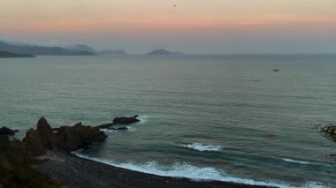 Top view of the rocky seashore, cliff, waves roll to the shore, sea foam. 4k