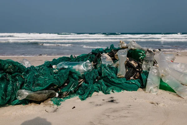 Plastic bottles and other rubbish thrown on the sandy seashore, trash on the sea beach. ecological problem. Environmental pollution. Dirty sandy beach. Old fishing net thrown to the seashore,