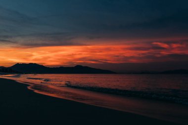 Güzel bir gün doğumu, bulutların arasından güneşin batışı, bulutların arasından güneş ışınları, küçük dalgalarla kumlu deniz kıyıları, denize yakın tropikal bir bölgede sıcak bir sabah ışığı..