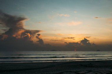 Güzel bir gün doğumu, bulutların arasından güneşin batışı, bulutların arasından güneş ışınları, küçük dalgalarla kumlu deniz kıyıları, denize yakın tropikal bir bölgede sıcak bir sabah ışığı..