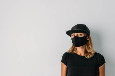 Salgın, koronavirüs, koruyucu maskeli bir kadın, hastalığın yayılmasına karşı. COVID-19. Evde karantina var. Siyah maskeli, siyah tişörtlü ve şapkalı bir kadın. Yan tarafa bak, boşluğu kopyala