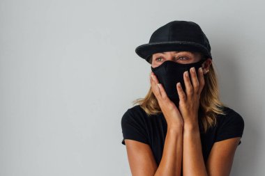 Salgın, koronavirüs, koruyucu maskeli bir kadın, hastalığın yayılmasına karşı. COVID-19. Evde karantina var. Siyah maskeli, siyah tişörtlü ve şapkalı bir kadın. Yan tarafa bak, boşluğu kopyala