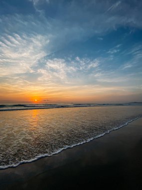Denizde şafak vakti ufuk manzarası, güneş ışınlarından renkli gökyüzü, mavi gökyüzündeki bulutlar. Deniz kıyısındaki kumsal, denizdeki dalgalar, fotokopici