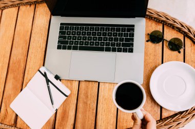 Dizüstü bilgisayarda çalışmak, kahverengi ahşap bir masa, bir fincan kahve ve kayıt için bir defter. Serbest meslek kavramı. Uzaktan kumanda. Yer kopyala