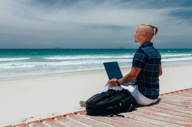 Genç serbest çalışan bir adam kumsalda deniz kıyısında dizüstü bilgisayar kullanarak içerik çalışma planı yapar. Uzaktan kumandalı bir yolculuk üzerinde çalışan bir iş adamı. Blogcu, deniz kenarına bakıyor