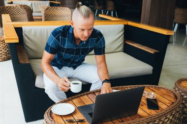 Genç bir adam bir kafede oturuyor, elinde bir fincan kahve tutuyor, mesajı laptoptan kontrol ediyor ve bir cevap mektubu yazıyor. Morning Post. Bakışlar ekrana yönlendirilir.