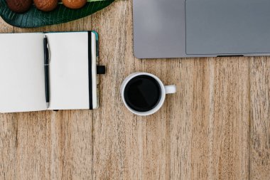 İşyerinin düzlüğü. Serbest çalışan, bilgisayarlı, akıllı telefon ve not defteri. Kurabiyeli sabah kahvesi. Boşluğu tahta arka plan ve not defterine kopyala. Üst görünüm, dizüstü bilgisayarın yanında bir defter, kayıt için bir kalem. Metin için yer