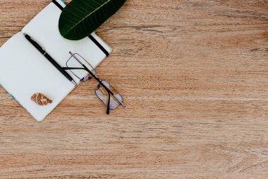 Düz yatıyordu, açık beyaz bir defterin üst görüntüsü, açık tahta bir masanın üzerine o gün için kutu yazmak için kalemle. Çalışma yüzeyi, metin için boş yer, defterin yanında gözlük, masada yeşil sayfa, boşluğu kopyala